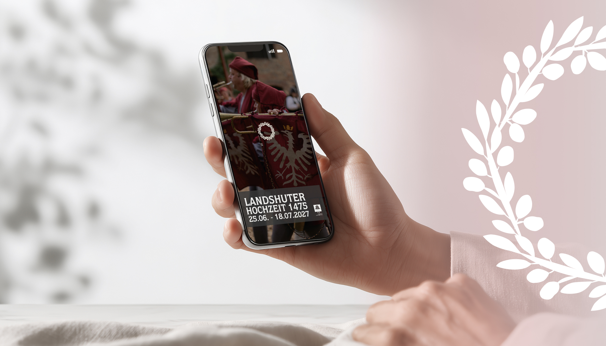 Eine Hand hält ein Smartphone, das Informationen zur Landshuter Hochzeit 1475 zeigt. | © madmoses